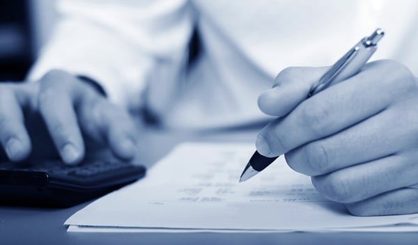 A hand working a calculator while the other hand writes figures on a sheet of paper.